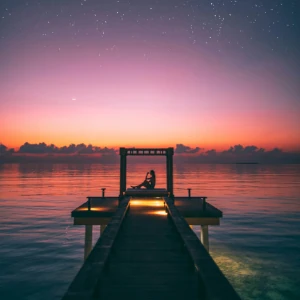 pier surrounded by dark waters and a glowing sky