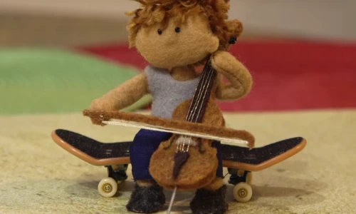 stop-motion image of felt doll playing the cello on a skateboard